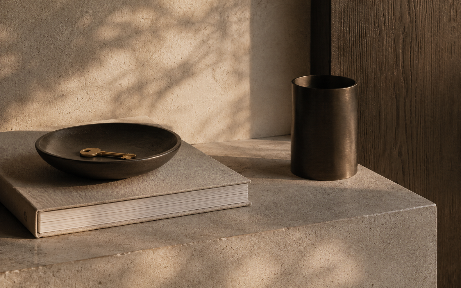 Brass key resting in a dark tray on a linen-bound book and textured stone surface.